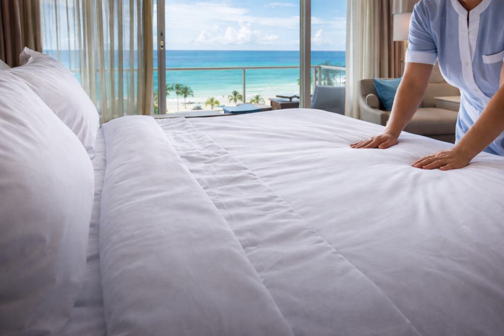 Housekeeper making a resort bed with fresh white linens overlooking the Gulf